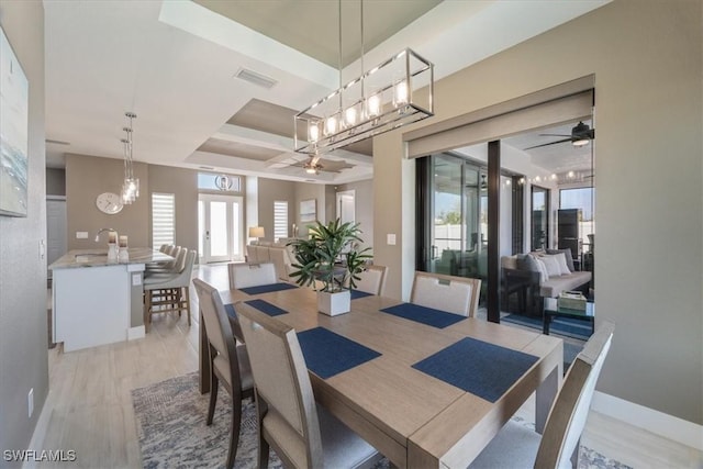 dining room featuring visible vents, a raised ceiling, light wood-style floors, and a healthy amount of sunlight