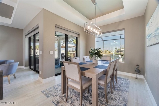 dining area with baseboards, a raised ceiling, light wood-style flooring, and ceiling fan with notable chandelier