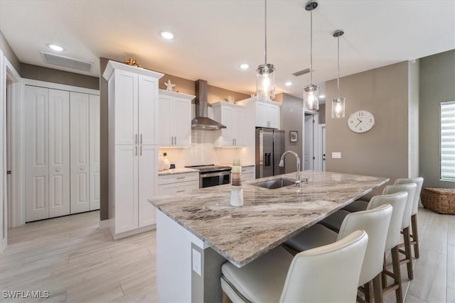 kitchen featuring a sink, stainless steel appliances, wall chimney exhaust hood, and white cabinetry