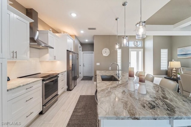 kitchen with visible vents, appliances with stainless steel finishes, a large island, wall chimney exhaust hood, and a sink