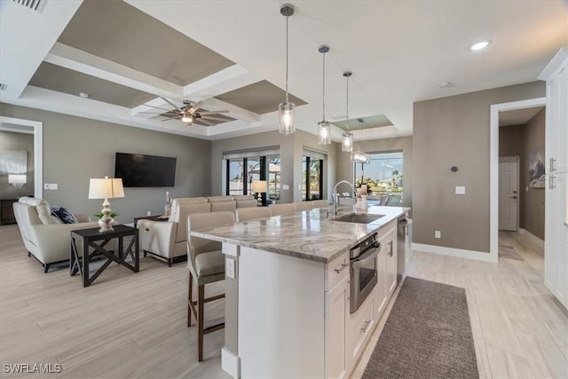 kitchen with a center island with sink, a sink, white cabinets, stainless steel oven, and light stone countertops