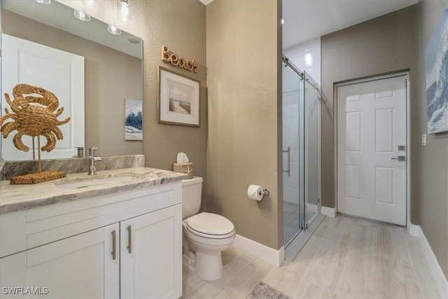 bathroom with a shower stall, baseboards, toilet, wood finished floors, and vanity