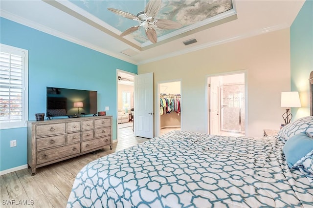 bedroom featuring ceiling fan, a raised ceiling, crown molding, a walk in closet, and a closet