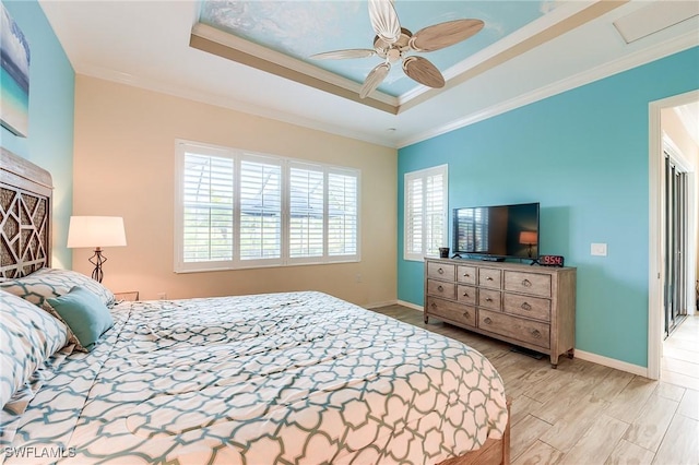 bedroom with ceiling fan, a tray ceiling, ornamental molding, and light wood-type flooring