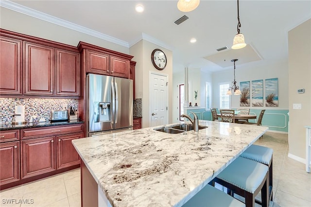 kitchen with sink, stainless steel fridge, a kitchen island with sink, and dark stone counters