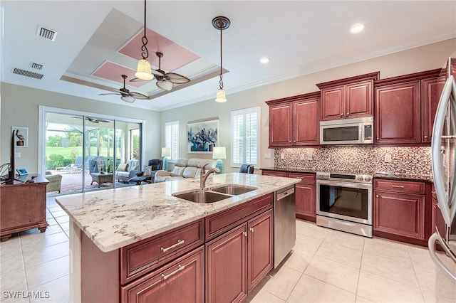 kitchen featuring appliances with stainless steel finishes, a tray ceiling, a kitchen island with sink, hanging light fixtures, and sink