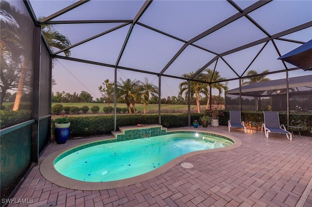 pool at dusk featuring pool water feature, a patio, and glass enclosure