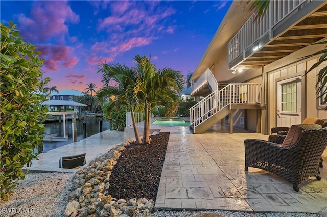 patio terrace at dusk with a water view, a balcony, and a dock