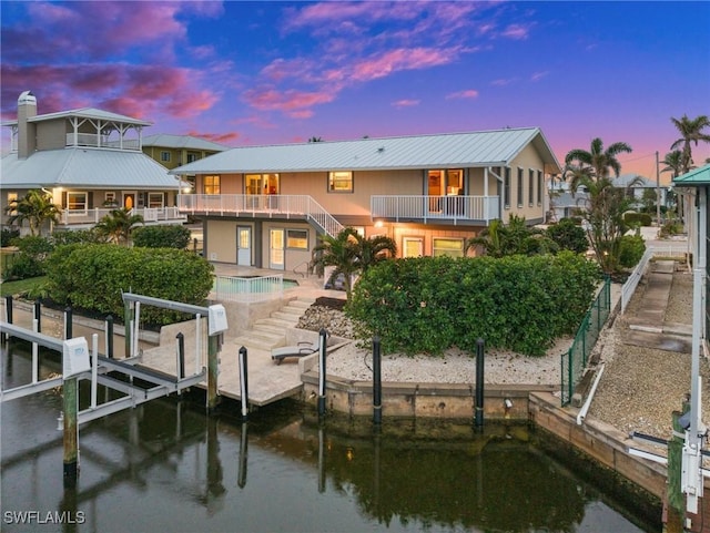 back house at dusk featuring a patio, a fenced in pool, a balcony, and a water view