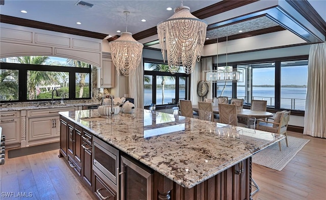 kitchen with stainless steel microwave, beverage cooler, a notable chandelier, a water view, and ornamental molding