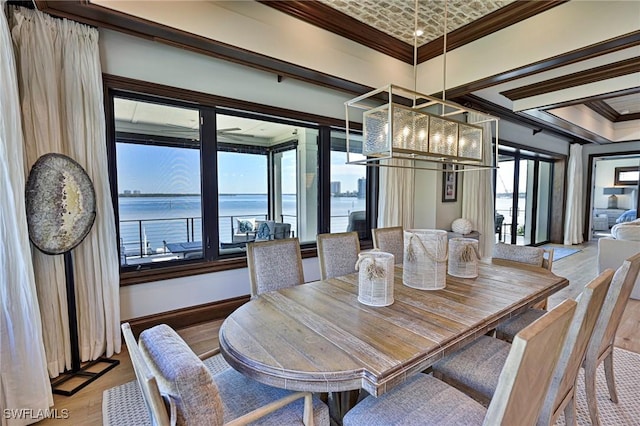 dining space featuring light wood-type flooring, a water view, an inviting chandelier, and ornamental molding