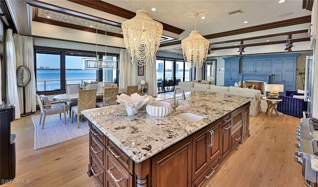 kitchen with a water view, a kitchen island with sink, crown molding, and sink