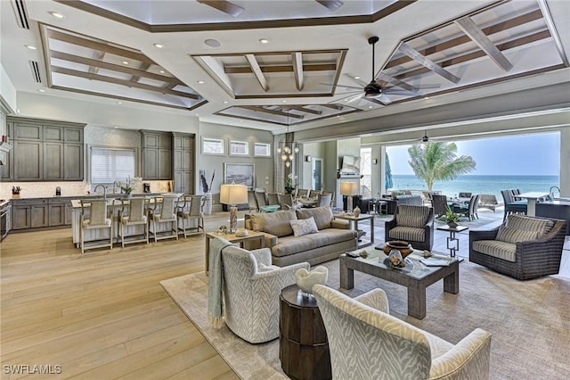 living area featuring light wood-style flooring, a water view, coffered ceiling, a towering ceiling, and a ceiling fan