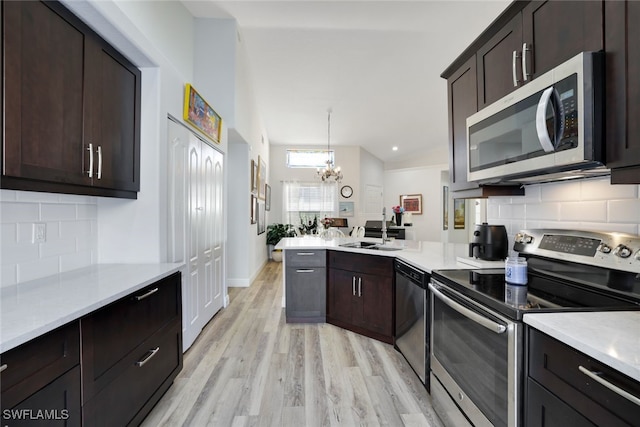 kitchen featuring tasteful backsplash, an inviting chandelier, light wood-type flooring, and appliances with stainless steel finishes