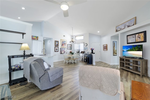 living room featuring ceiling fan with notable chandelier, light wood-type flooring, sink, and vaulted ceiling