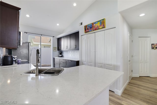 kitchen with sink, light hardwood / wood-style flooring, backsplash, kitchen peninsula, and vaulted ceiling