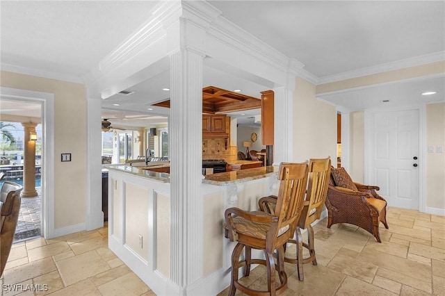 kitchen featuring sink, light stone counters, kitchen peninsula, crown molding, and a breakfast bar