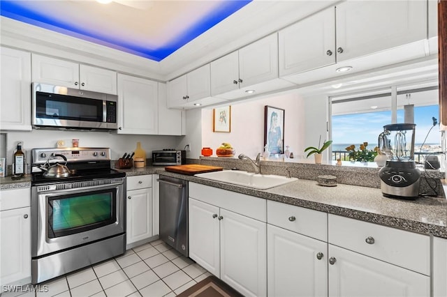 kitchen with light tile patterned flooring, stainless steel appliances, a sink, white cabinets, and dark countertops