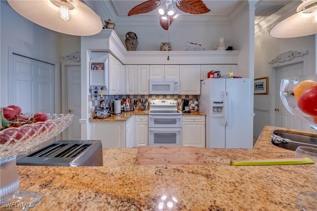 kitchen with tasteful backsplash, light stone counters, crown molding, white appliances, and white cabinets