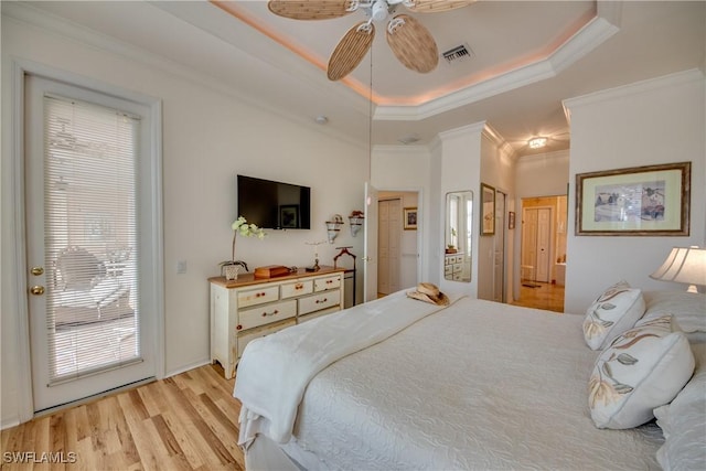 bedroom featuring a tray ceiling, ceiling fan, crown molding, and light wood-type flooring