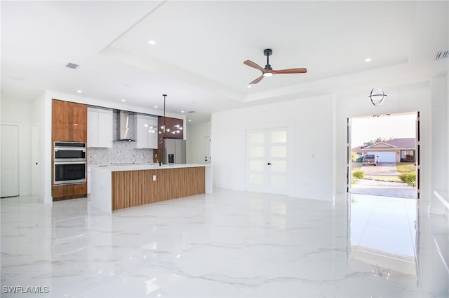 kitchen featuring appliances with stainless steel finishes, a tray ceiling, decorative light fixtures, and an island with sink