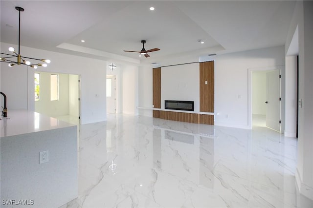 unfurnished living room with a raised ceiling and ceiling fan with notable chandelier