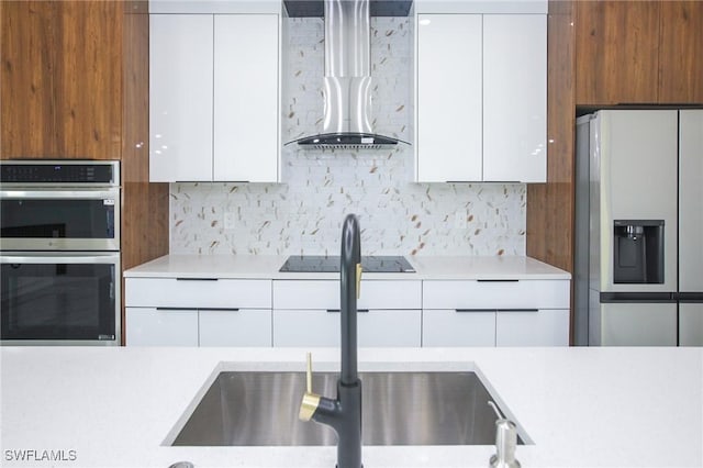 kitchen with wall chimney range hood, sink, decorative backsplash, appliances with stainless steel finishes, and white cabinetry