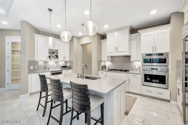 kitchen featuring hanging light fixtures, backsplash, an island with sink, white cabinets, and appliances with stainless steel finishes