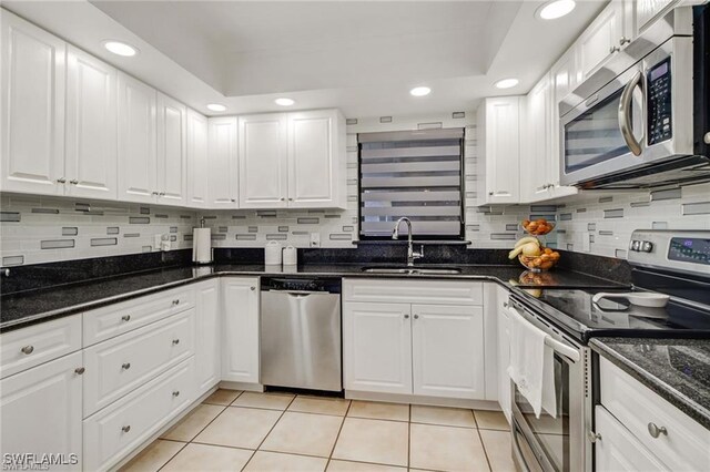 kitchen with dark stone counters, white cabinets, sink, light tile patterned floors, and stainless steel appliances