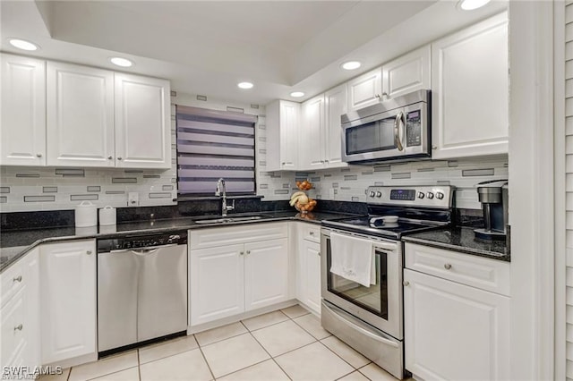 kitchen with white cabinetry, sink, dark stone countertops, light tile patterned floors, and appliances with stainless steel finishes