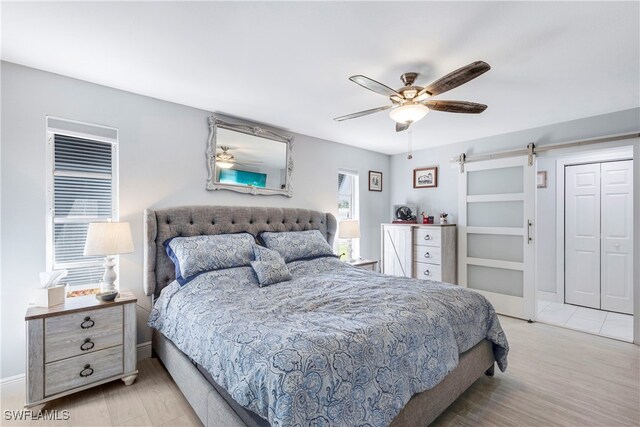 bedroom with ceiling fan, a barn door, light wood-type flooring, and a closet