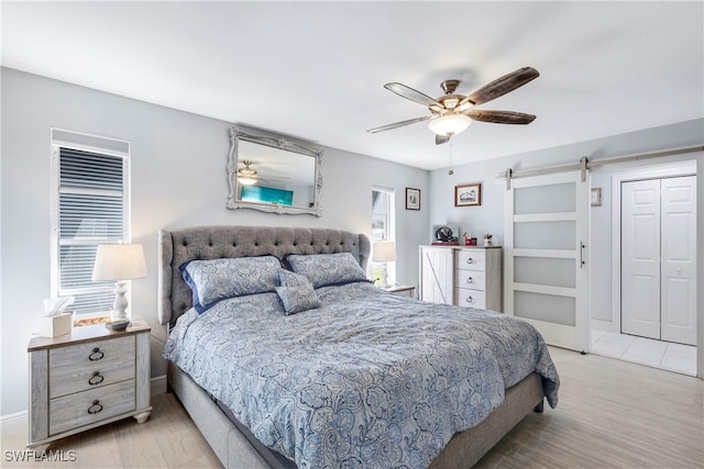 bedroom featuring ceiling fan, a barn door, light wood-style flooring, baseboards, and a closet