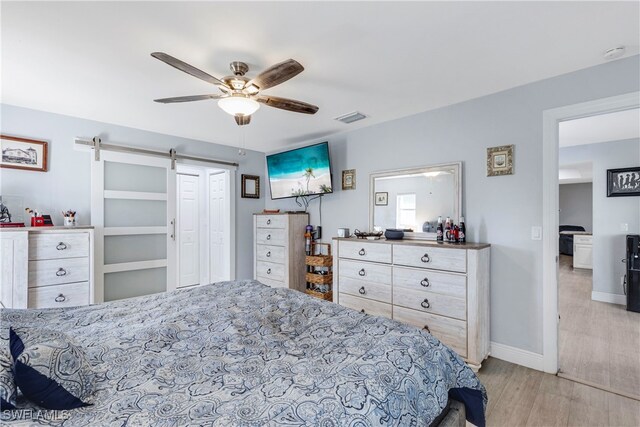 bedroom with a barn door, a ceiling fan, visible vents, baseboards, and light wood finished floors