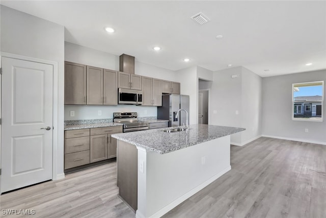 kitchen with light stone counters, stainless steel appliances, sink, light hardwood / wood-style floors, and an island with sink