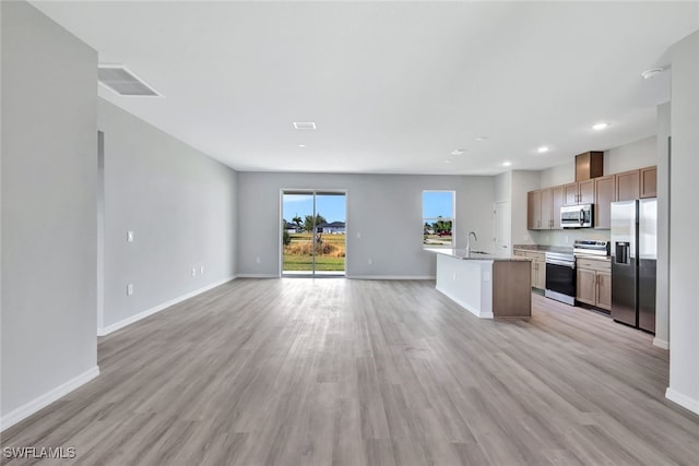 kitchen with light hardwood / wood-style floors, sink, stainless steel appliances, and an island with sink