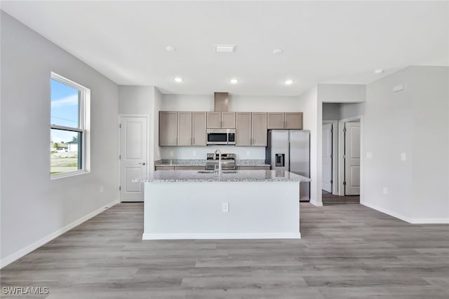 kitchen with light stone countertops, appliances with stainless steel finishes, sink, hardwood / wood-style floors, and an island with sink