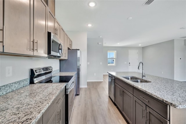 kitchen with sink, stainless steel appliances, light stone counters, light hardwood / wood-style flooring, and a center island with sink