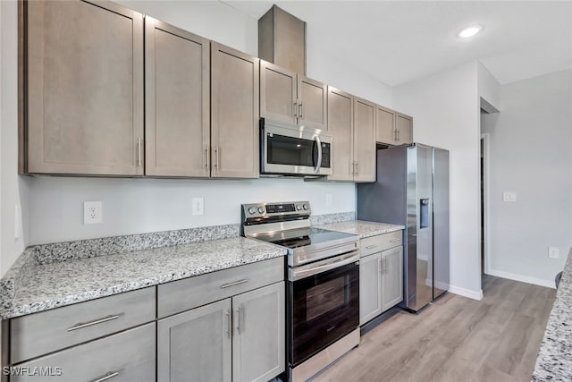 kitchen with light stone countertops, appliances with stainless steel finishes, and light hardwood / wood-style flooring