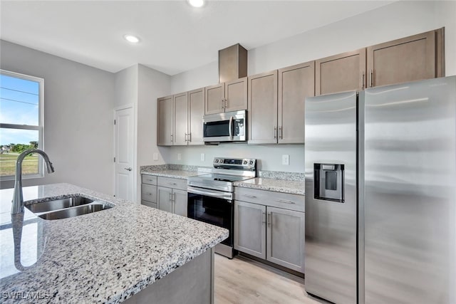 kitchen featuring light stone countertops, appliances with stainless steel finishes, light hardwood / wood-style floors, and sink