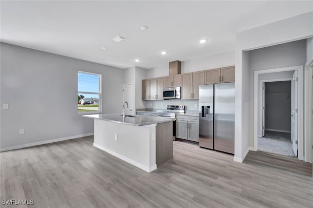 kitchen with sink, stainless steel appliances, light stone counters, light hardwood / wood-style floors, and a center island with sink