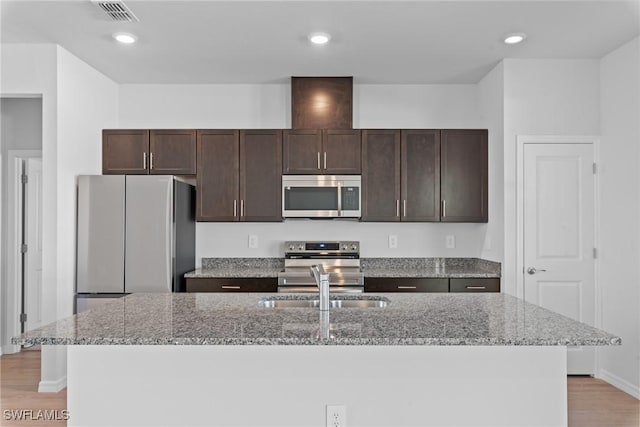 kitchen with light stone countertops, an island with sink, and appliances with stainless steel finishes