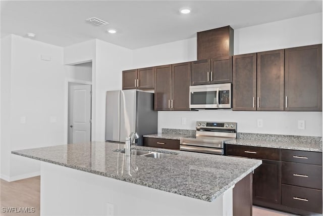 kitchen with a kitchen island with sink, light stone counters, sink, and stainless steel appliances