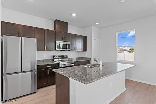 kitchen featuring a center island with sink, sink, light stone countertops, light hardwood / wood-style floors, and stainless steel appliances