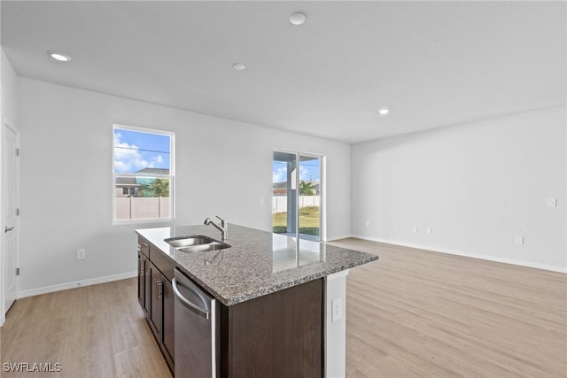 kitchen with a center island with sink, sink, light hardwood / wood-style flooring, light stone counters, and dark brown cabinetry