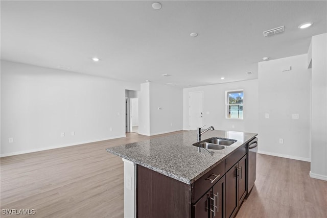 kitchen with a kitchen island with sink, sink, stainless steel dishwasher, light stone countertops, and dark brown cabinets