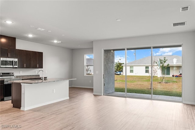 kitchen with a wealth of natural light, dark brown cabinetry, an island with sink, and appliances with stainless steel finishes