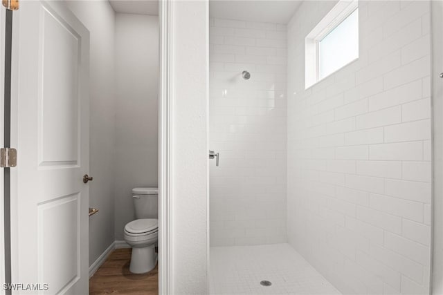 bathroom featuring a tile shower, wood-type flooring, and toilet