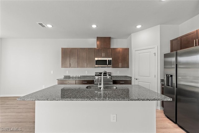 kitchen with sink, stainless steel appliances, dark stone counters, and an island with sink