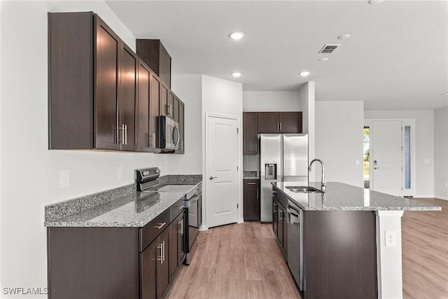 kitchen with a kitchen island with sink, sink, stainless steel appliances, and light stone counters