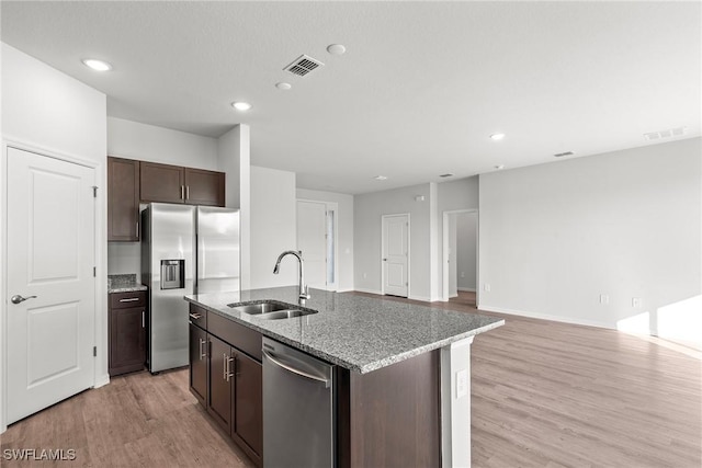 kitchen featuring light stone countertops, sink, stainless steel appliances, dark brown cabinets, and a center island with sink